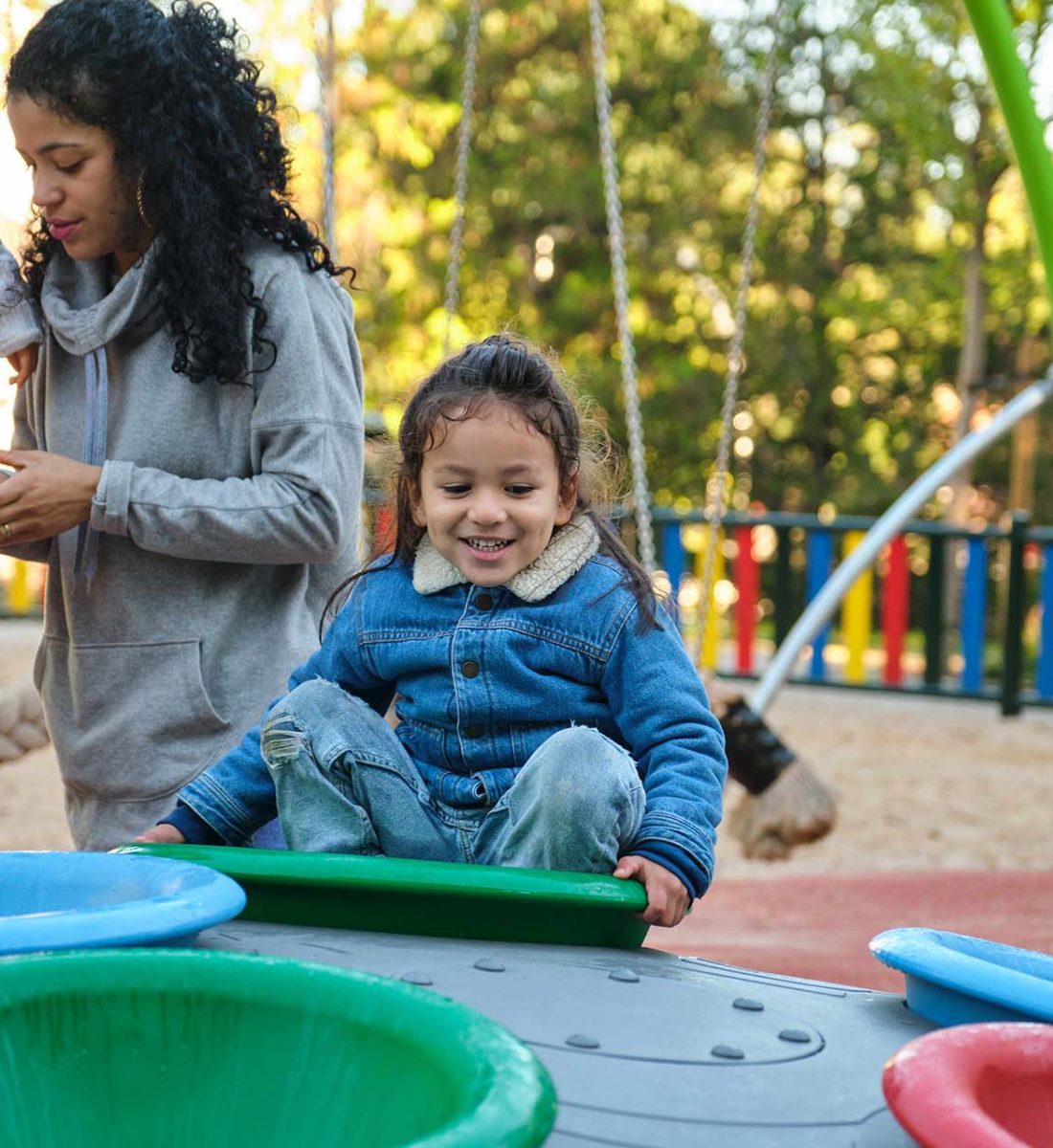 Latin boy playing in a playground, his family on the background. Hispanic family.