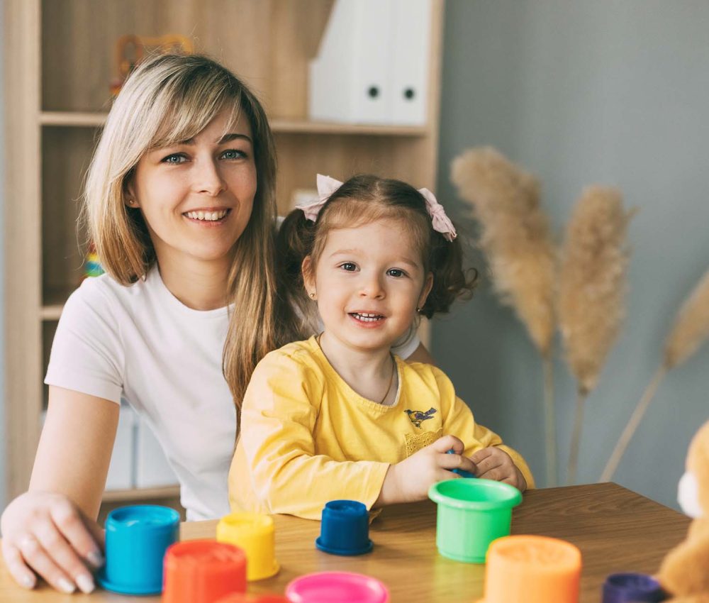 Portrait of a young mother and her little daughter playing at a table with colorful molds. Time together, motherhood, parenthood.